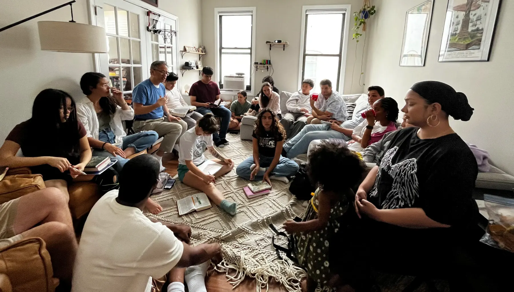 A room full of people sitting on couches and the floor with open Bibles, talking together